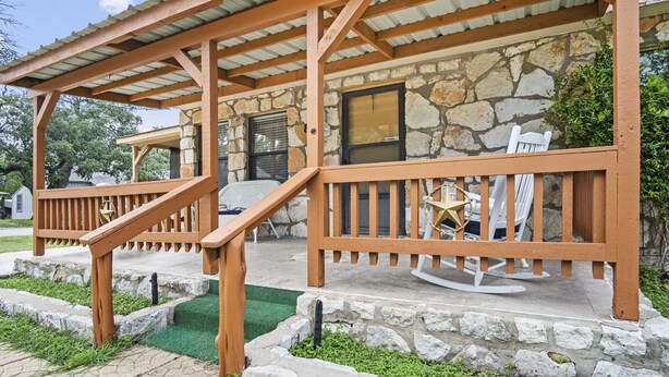 A covered outdoor area with a wooden deck, stone walls, and a stone fireplace.