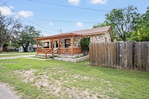 A single-story stone house with a wooden porch and a fenced yard.