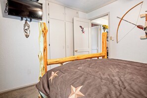 A bedroom with a bed, a television mounted on the wall, and a wardrobe. - The Lazy Spur | Cozy 2BR Cabin in Cowboy Capital (Bandera)