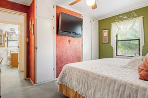 A bedroom with a bed, a television mounted on a wall, a window with curtains, and a door leading to a bathroom. - The Lazy Spur | Cozy 2BR Cabin in Cowboy Capital (Bandera)
