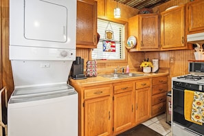 A compact kitchen with wooden cabinets, a white stove, a sink, and a coffee maker.