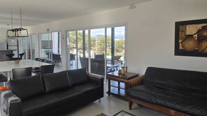 A modern living room with a black leather sofa, a glass coffee table, and a dining area with a white table and chairs. - "PARADISE". (Coronel Moldes)