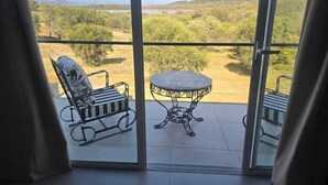 A balcony with a metal chair and a small table, offering a view of a natural landscape with trees and hills. - "PARADISE". (Coronel Moldes)