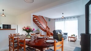 A modern living room with a dining area, a staircase, and a wood-burning stove. - Ty Kroesi - La maison du port (Arzon)
