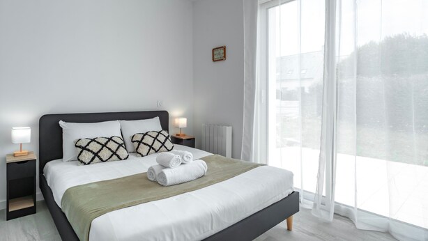 A modern bedroom with a large bed, white bedding, and a view of the outdoors through sheer curtains. - Ty Kroesi - La maison du port (Arzon)