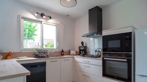A modern kitchen with white cabinets, a dishwasher, a coffee maker, and a built-in oven. - Ty Kroesi - La maison du port (Arzon)