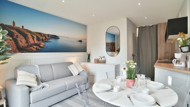 A modern living room with a grey sofa, a dining table set for four, and a large coastal mural on the wall. - Lya 04 - 5min à Pied de la Plage (Fréhel)