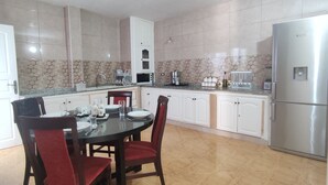 A modern kitchen with white cabinets, a stainless steel refrigerator, a dining table with chairs, and a microwave.