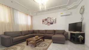A living room with a sectional sofa, a coffee table, a flat-screen TV, and a decorative wall piece.
