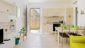 Un apartamento moderno con sala de estar, cocina y comedor. Hay un televisor, una pequeña mesa con sillas y un sofá verde brillante.