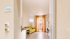 Habitación de hotel con cama, escritorio y silla. Cuenta con una ventana con cortinas y una puerta que da a otra habitación.