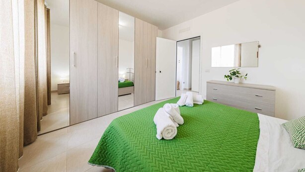 Un dormitorio moderno con colcha acolchada verde, un espejo grande y un vestidor.