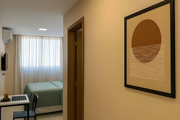 A hotel room with a bed, a desk with a chair, a framed artwork on the wall, and a window with curtains. - Varandas do Porto (Ipojuca)