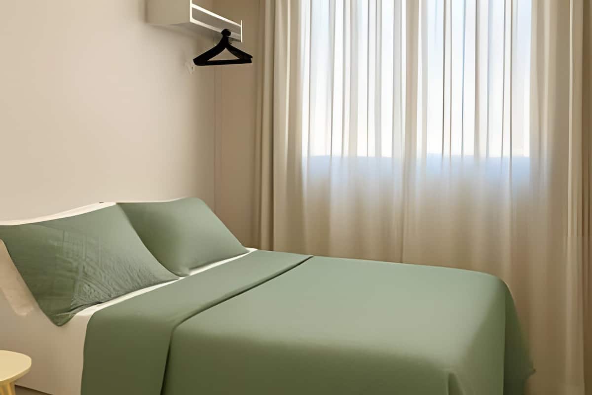 A neatly arranged bedroom with a bed, a chair, a small table, and a hanging light fixture.