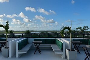 Terraza en la azotea con asientos y mesas verdes, con vistas a un paisaje de agua y colinas.