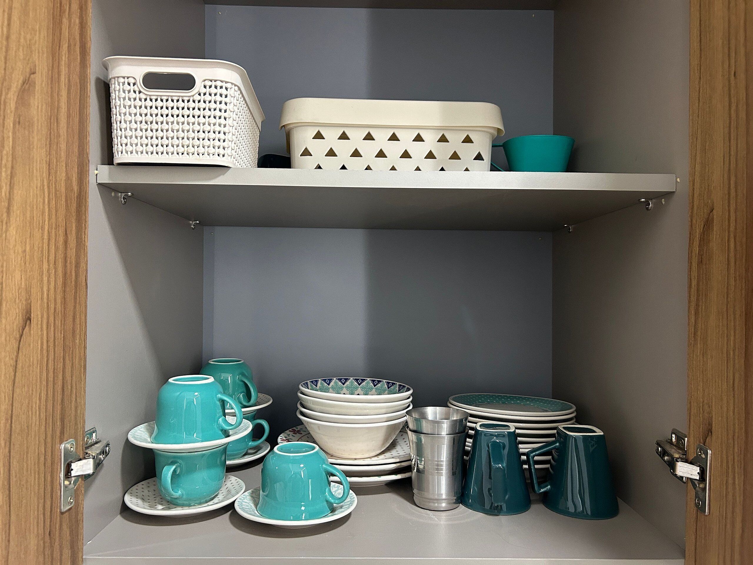 Una cucina con mensole bianche che contengono diversi utensili da cucina, tra cui tazze, piatti e un cesto.