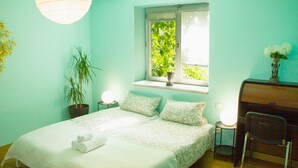 Ein Schlafzimmer mit Bett, Nachttischen, Schreibtisch, Stuhl, Fenster mit Blick auf Grünflächen und einer Hängeleuchte.