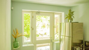 Eine Küche mit Kühlschrank, einem Fenster mit Blick auf Grünflächen und einer Vase mit Blumen auf einem Stuhl.