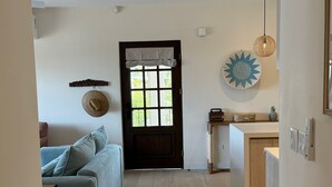 A cozy living room with a sofa, a door leading to a kitchen, and a decorative wall piece. - Oceanview Apt, 3BR/2BA in The Catalinas, 5 min walk to the beach, free parking (Las Catalinas)