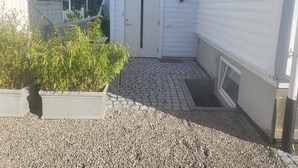 A small, enclosed outdoor area with a gravel ground, a potted plant, and a door leading to a building with white siding.