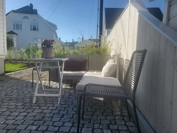A patio with a table and chairs, a wicker sofa, and a potted plant.
