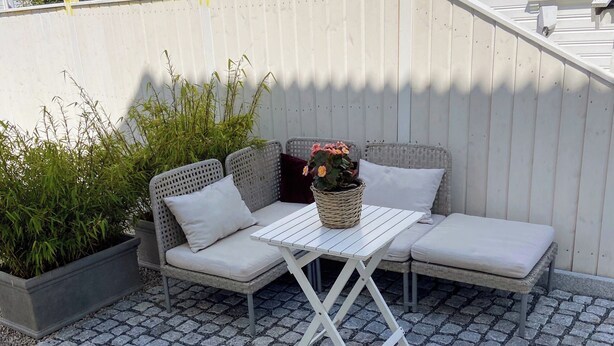 A white outdoor seating area with a table and cushions, surrounded by potted plants and a white fence.