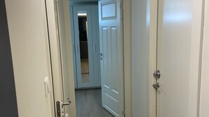 A hallway with wooden flooring, a white door on the right, and a partially open door leading to another room.