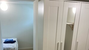 A room with a wardrobe, a bed, and a small shelf.