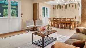A spacious living room with a dining area, large windows, and a view of greenery outside. - Gîtes de France® - Green Station (FORGES LES EAUX)