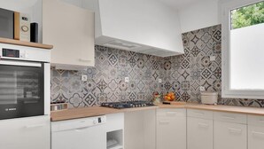 A modern kitchen with white cabinets, a Bosch oven, a built-in microwave, and a patterned backsplash. - Gîtes de France® - Green Station (FORGES LES EAUX)