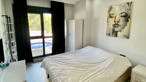 A modern bedroom with a large bed, a wardrobe, a desk, and a bathroom. - Stylish 1BR Flat Pool View & 10 min Walk to Beach (Avsallar)