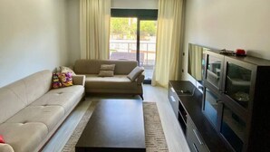 A living room with a sofa, a coffee table, a TV, and a cabinet. - Stylish 1BR Flat Pool View & 10 min Walk to Beach (Avsallar)