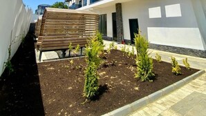 A modern multi-story building with balconies, a garden area with small plants, and a wooden structure. - Stylish 1BR Flat Pool View & 10 min Walk to Beach (Avsallar)