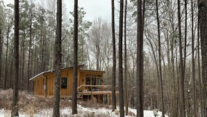 Une cabane dans une forêt, dotée d’une terrasse en bois et d’un petit porche.