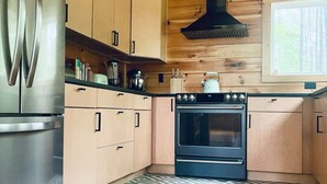 Une cuisine avec des meubles de rangement en bois, un réfrigérateur en acier inoxydable, une cuisinière noire et des carreaux de sol à motifs.