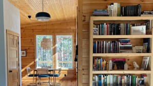 L’intérieur chaleureux d’un chalet avec une bibliothèque en bois, un coin repas et une vue sur l’extérieur grâce à de grandes fenêtres.