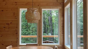 L’intérieur d’un chalet en bois comprend une table à manger, des chaises et de grandes fenêtres donnant sur la forêt.