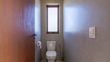 A small bathroom with a toilet, a window, and a shower.
