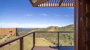 A wooden deck with a metal railing overlooking a hilly landscape.