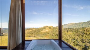 A room with a large window offering a view of rolling hills and a clear sky. - Cabana rústica com jacuzzi VST003 (Anitápolis)