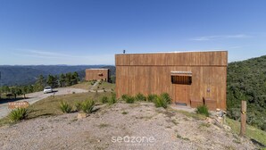 A modern wooden cabin with a large door and a small window, surrounded by a gravel driveway and a sign reading "GARAGEM 43". - Cabana rústica com jacuzzi VST003 (Anitápolis)