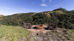 Un camping con dos sillas de madera y un brasero circular en una colina cubierta de hierba.