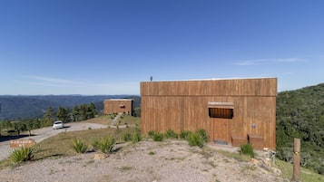 Una cabaña moderna de madera con una puerta grande y una ventana pequeña, rodeada por un camino de grava y un letrero que dice "GARAGEM 43".