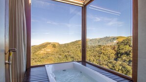 A bathroom with a large window offering a view of a forested hillside. - Cabana rústica com jacuzzi VST003 (Anitápolis)