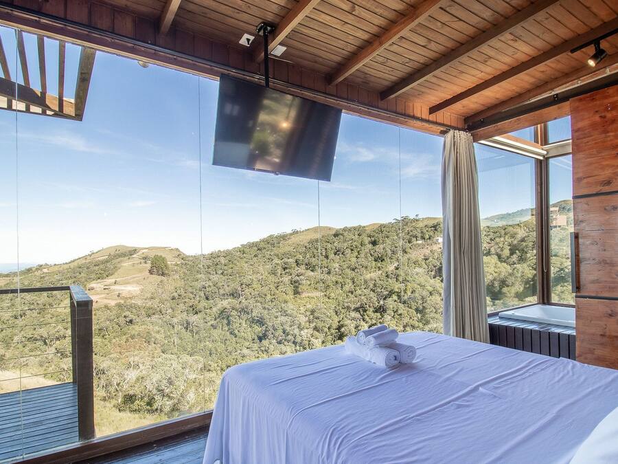 A bedroom with a large window overlooking a hilly landscape.