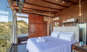 Une chambre avec un grand lit, un plafond en bois et une vue sur un paysage vallonné.
