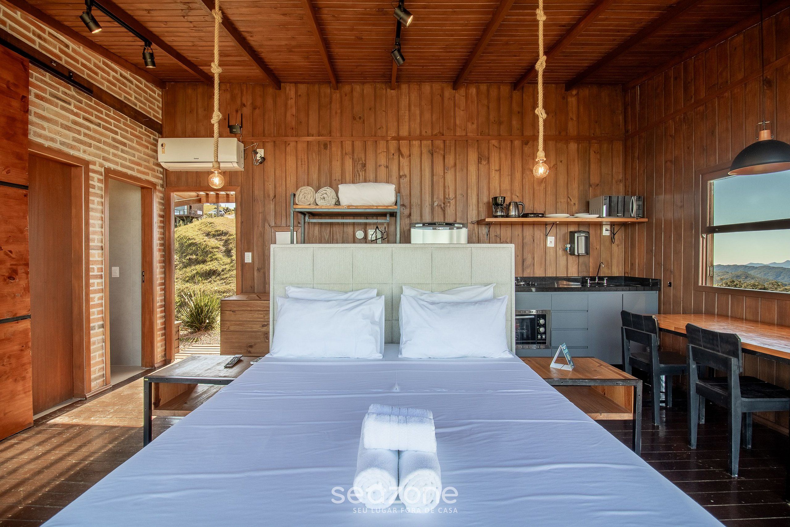 Een slaapkamer in een houten chaletstijl met een bed, nachtkastjes en uitzicht op de natuur.