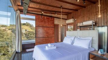 A bedroom with a large bed, wooden walls, a view of the outdoors, and a modern air conditioning unit.