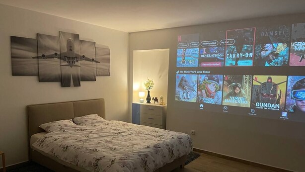 A bedroom with a bed, a wall-mounted projector displaying movie posters, and a nightstand with a lamp. - Tony's homestay in Strakonice 1+KK (Jihočeský kraj)