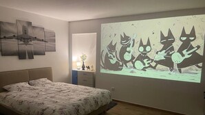 A bedroom with a bed, a projector screen displaying a cartoon, and a wall with abstract art. - Tony's homestay in Strakonice 1+KK (Jihočeský kraj)